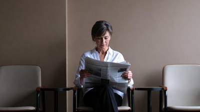 Elderly woman reading newspaper in waiting room