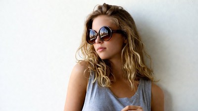 Blonde woman in sunglasses against wall