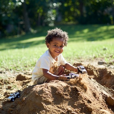 African-American toddler playing with toy trucks in sand