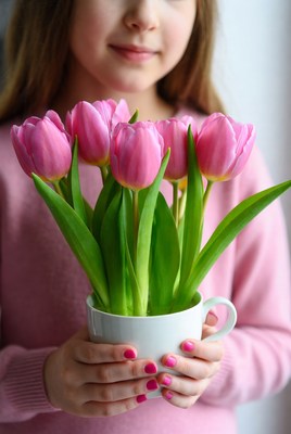 Girl holding pink tulips in cup