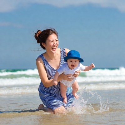 Asian mother holding laughing baby beach