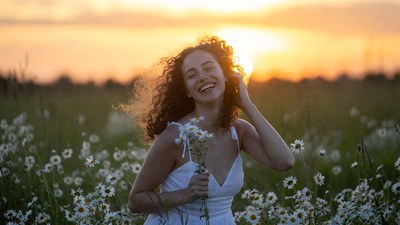 Smiling woman with daisies at sunset