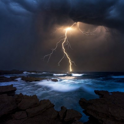Lightning striking over ocean rocks
