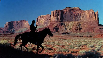 Cowboy riding horse silhouette against red rock mountains