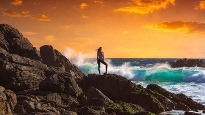 Woman standing on rocks at sunset ocean