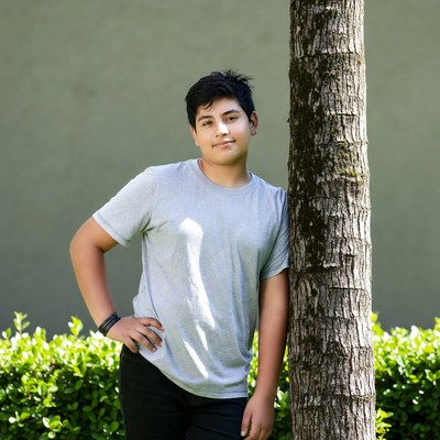 Latino teen boy leaning on tree