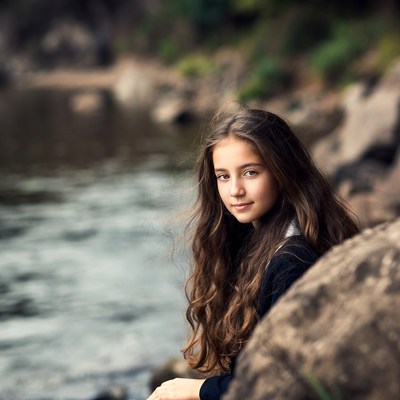 Girl sitting by river rocks