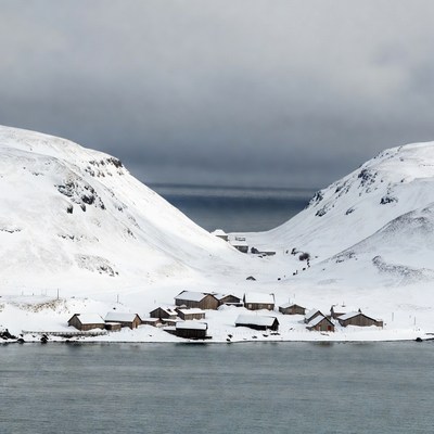 Snowy village between mountains by lake