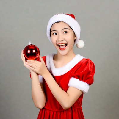 Asian girl in Santa dress holding red ornament