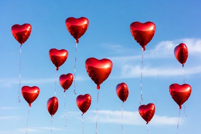 Red heart balloons floating in blue sky