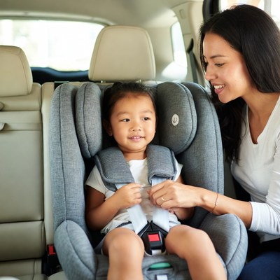 Mother buckling Asian toddler in car seat