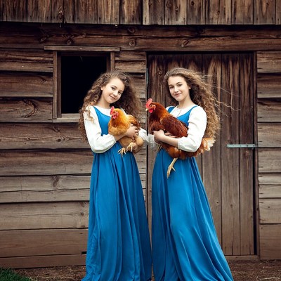 Twin girls holding chickens by wooden barn