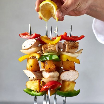 Hand Squeezing Lemon on Chicken Skewers