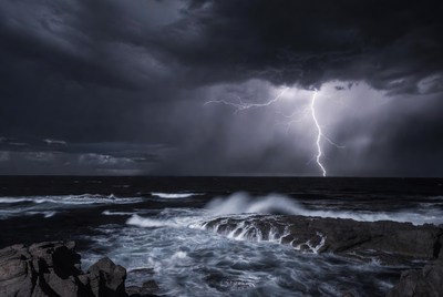Lightning striking over ocean rocks