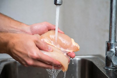 Man washing raw chicken under faucet