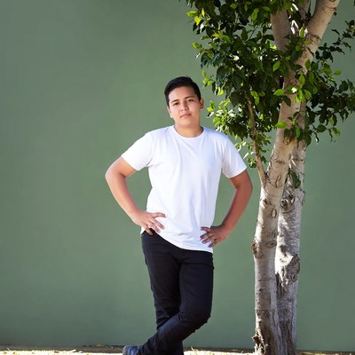 Latino teen boy posing by tree