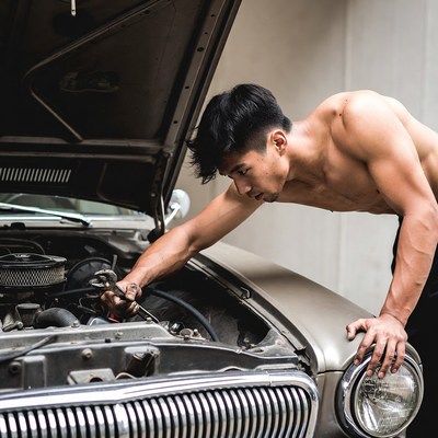 Shirtless Asian man repairing car engine