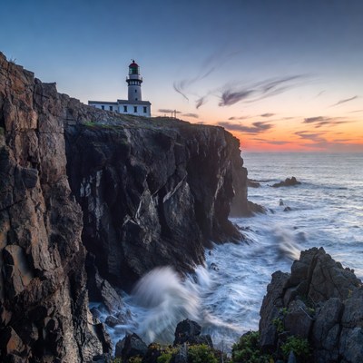 Lighthouse on rocky cliff at sunset