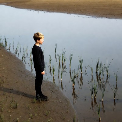 Boy standing by shallow water edge