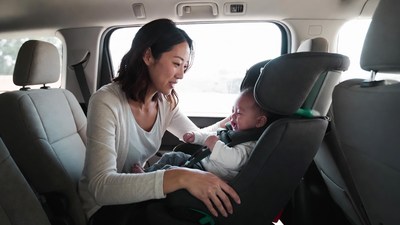Asian mother buckling baby in car seat