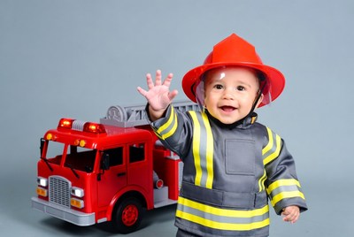 Baby boy waving in firefighter costume with toy truck