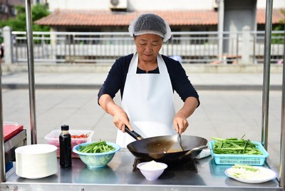 Asian woman stir-frying vegetables at street food stall