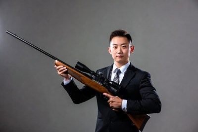 Asian man in suit holding sniper rifle