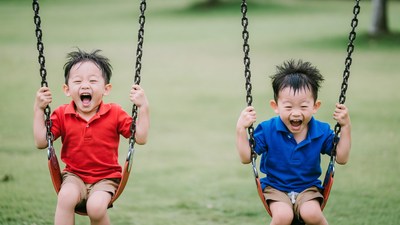 Twin Asian boys swinging on playground swings