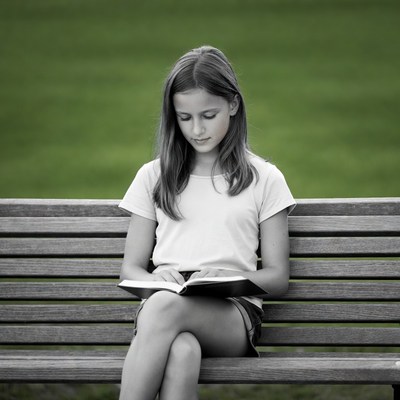 Girl reading book on park bench