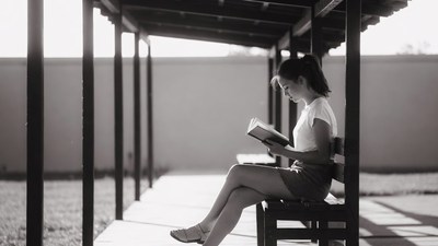 Asian woman reading book on bench