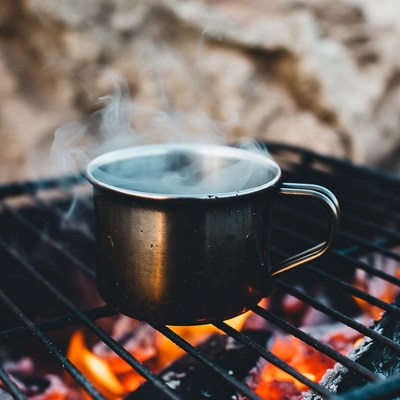 Steaming metal mug on campfire grill