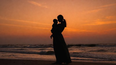 Silhouette of mother holding baby at sunset beach