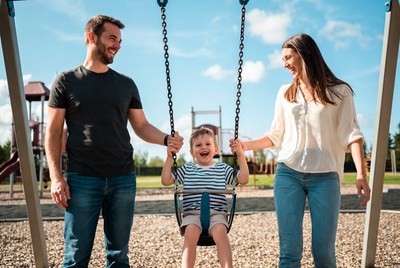Parents pushing toddler on playground swing