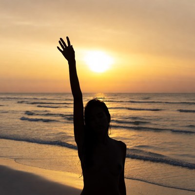 Silhouette of nude woman waving at sunset beach