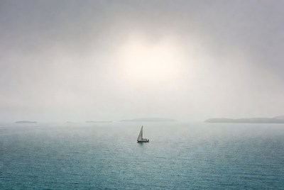 Sailboat in foggy sea with sun