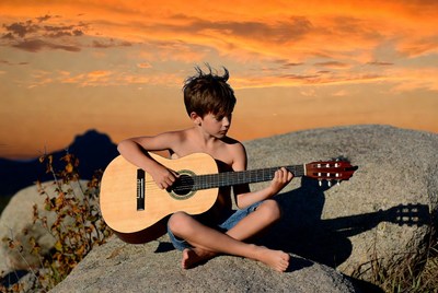 Boy playing guitar on rock at sunset