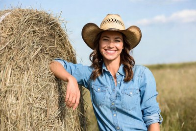 Smiling woman in cowboy hat by hay bale