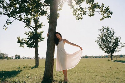 Woman leaning against tree in white dress