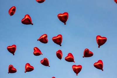 Red heart balloons floating in blue sky