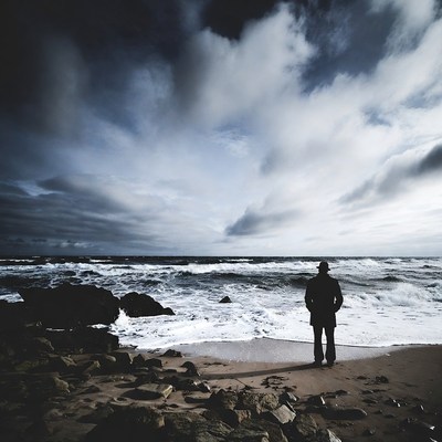 Man standing on beach facing stormy ocean
