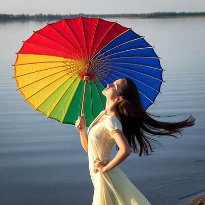 Woman holding rainbow umbrella by lake