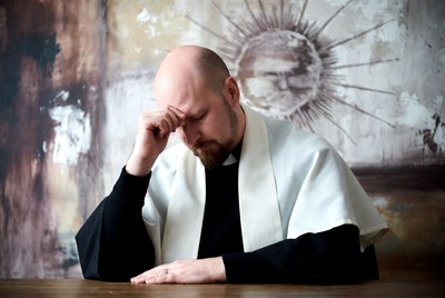 Bald priest rubbing forehead thoughtfully