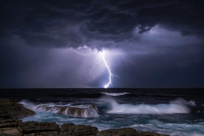 Lightning striking over ocean rocks