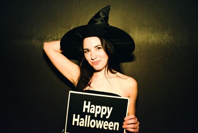 Woman in witch hat holding Happy Halloween sign