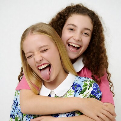 Blonde girl sticking tongue out hugged by curly-haired girl