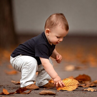 Baby boy picking up autumn leaf