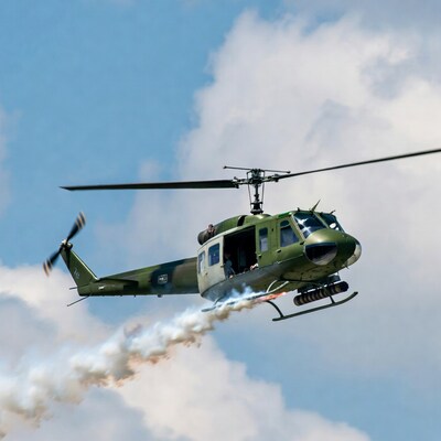 Green UH-1 Huey helicopter flying with smoke