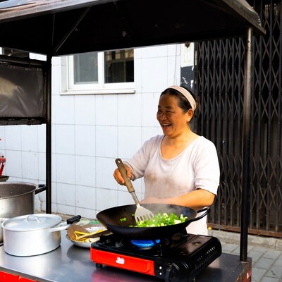 Asian woman stir-frying vegetables at street cart