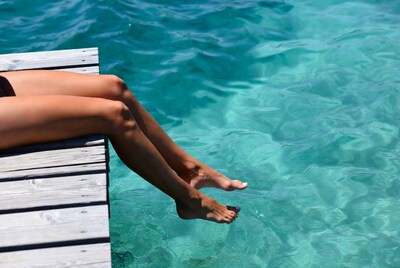 Woman's legs dangling over dock into turquoise water