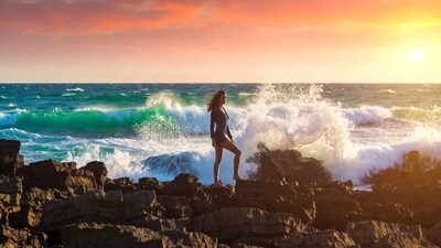 Woman standing on rocks by crashing waves sunset